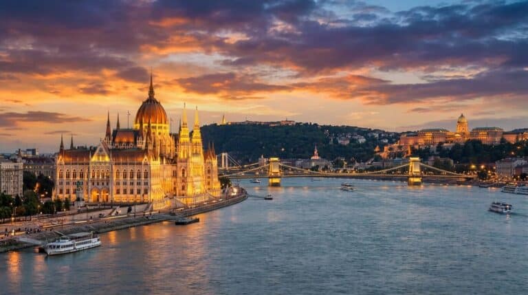 The Hungarian Parliament Building on the Danube River in Budapest, Hungary, is illuminated against a colorful sunset sky.
