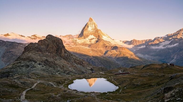The iconic Matterhorn mountain in Switzerland is reflected in a calm alpine lake during a colorful sunrise.