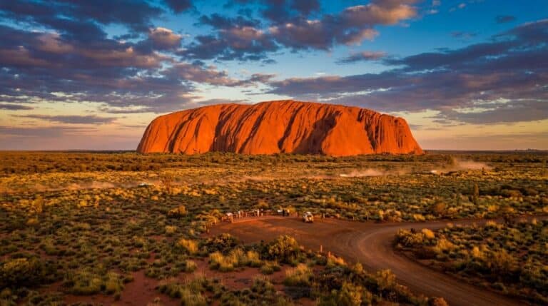 The massive sandstone monolith of Uluru glows a deep orange during sunset in the Australian outback.