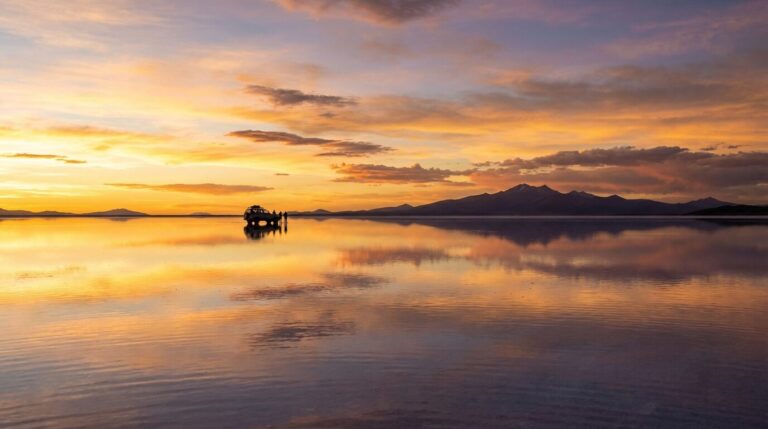 A vehicle and several people are silhouetted against a vibrant sunset over the Salar de Uyuni salt flats in Bolivia.