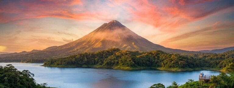Arenal Volcano in Costa Rica towers over the serene Lake Arenal during a beautiful, colorful sunset.