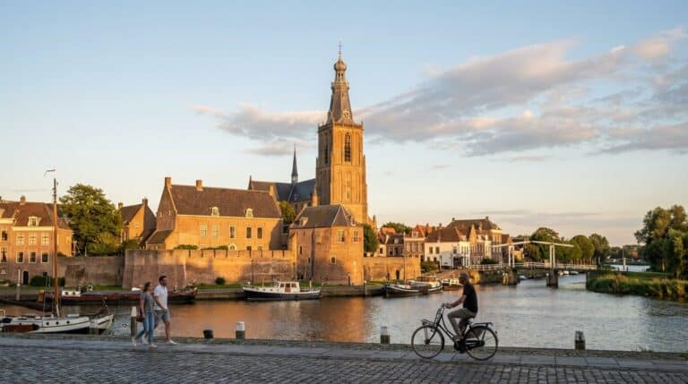 A scenic view across the harbor in Gorinchem at sunset, with the Grote Toren rising above historic buildings.