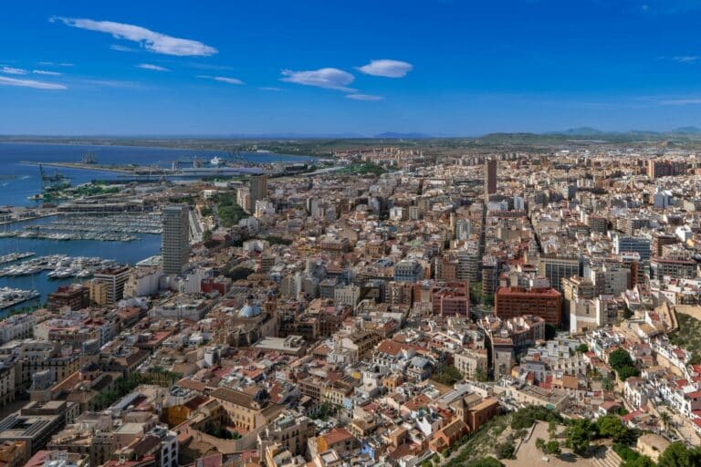 An expansive aerial view over the city of Alicante, with its bustling port, marina, and historic old town.