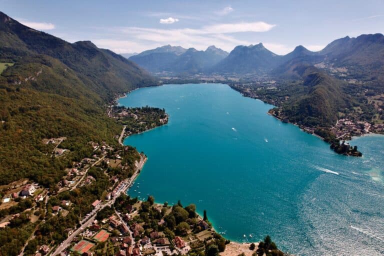 An aerial panoramic view of the turquoise waters of Lake Annecy surrounded by lush green mountains in France.