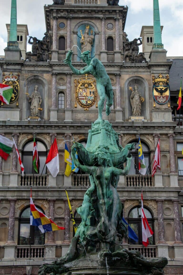 The iconic bronze Brabo Fountain stands majestically in front of the historic Antwerp City Hall building.