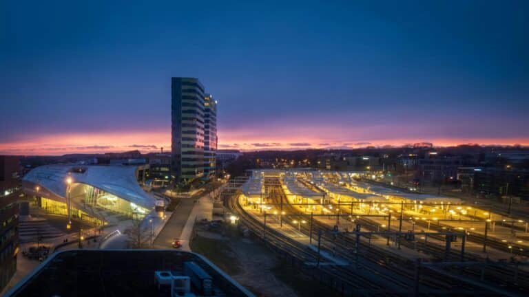 An elevated view of Arnhem Centraal station and the surrounding cityscape against a colorful twilight sky.
