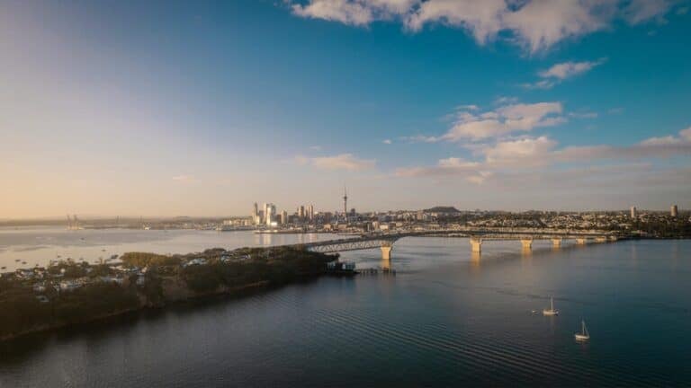 A scenic aerial view of the Auckland Harbour Bridge leading to the city skyline at sunset.
