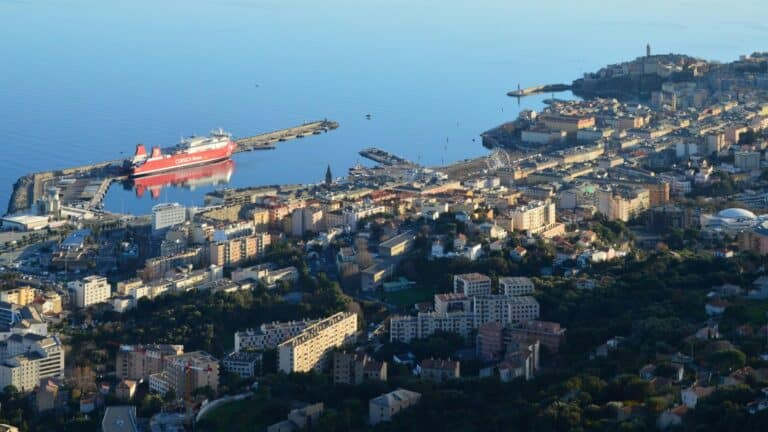 An elevated view of the coastal city of Bastia, showing the harbor with a large red ferry docked.