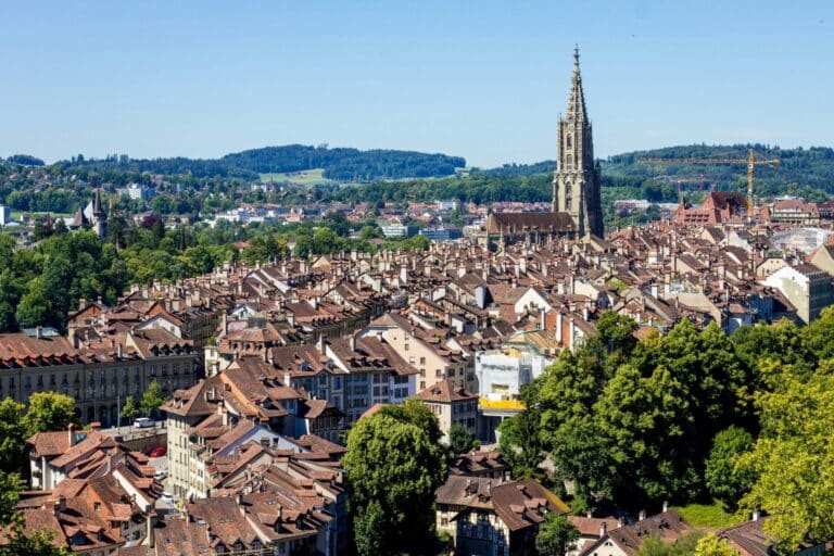 A high-angle view over the dense, red-tiled rooftops of the Old City of Bern and the towering Bern Minster.