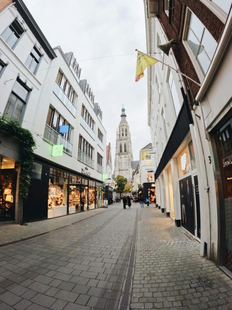 A wide-angle view down a cobblestone shopping street in Breda, leading towards the historic Grote Kerk tower.