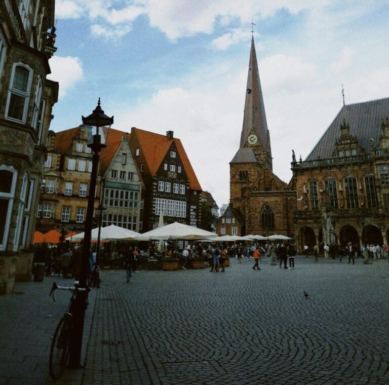 A view across the cobblestone Market Square in Bremen, showing the spire of the Liebfrauenkirche and other historic buildings.