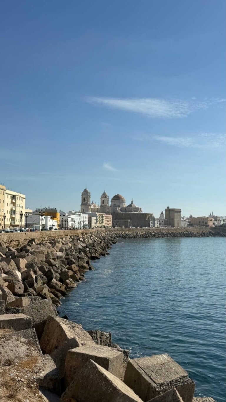 The Cádiz Cathedral and city skyline viewed from across the water behind the large rocks of the sea wall.