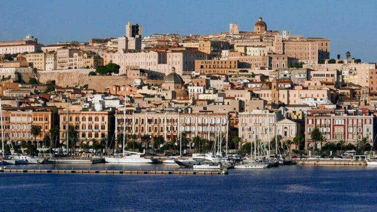 A panoramic view of the historic Castello district of Cagliari, Italy, seen from the bustling harbor.