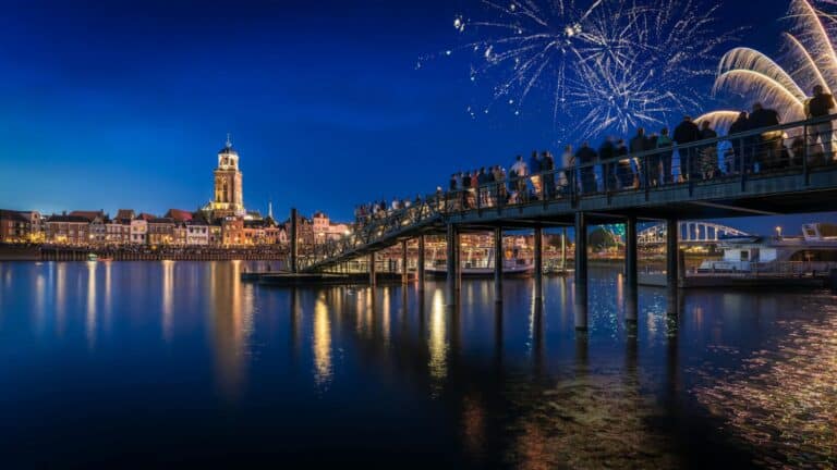 People watch a fireworks display over the IJssel river in Deventer, with the illuminated Lebuinuskerk in the background.