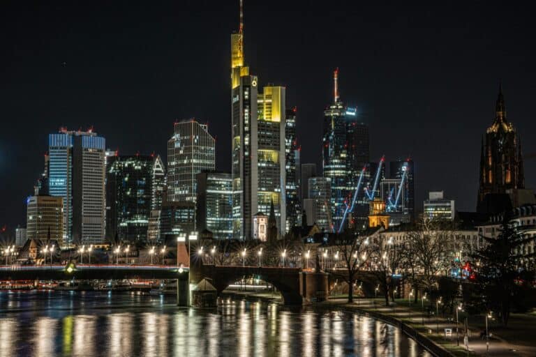 The Frankfurt skyline with its illuminated skyscrapers and cathedral reflected in the River Main at night.