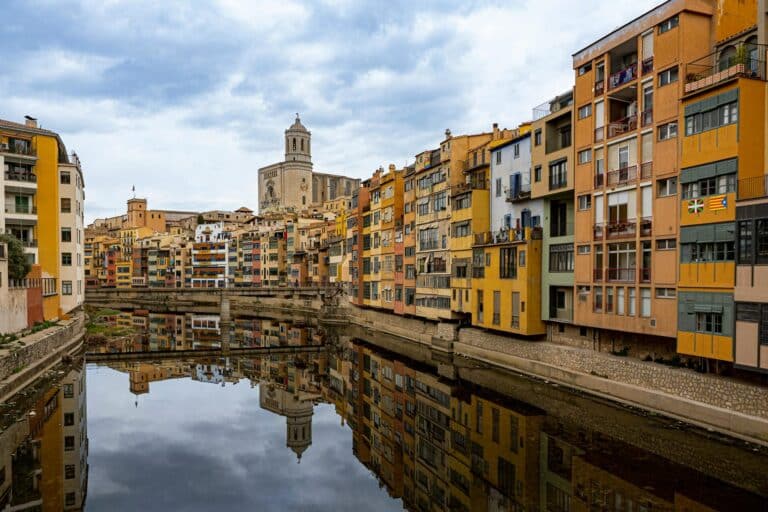Colorful houses and the Girona Cathedral reflected in the Onyar River on a cloudy day in Girona, Spain.