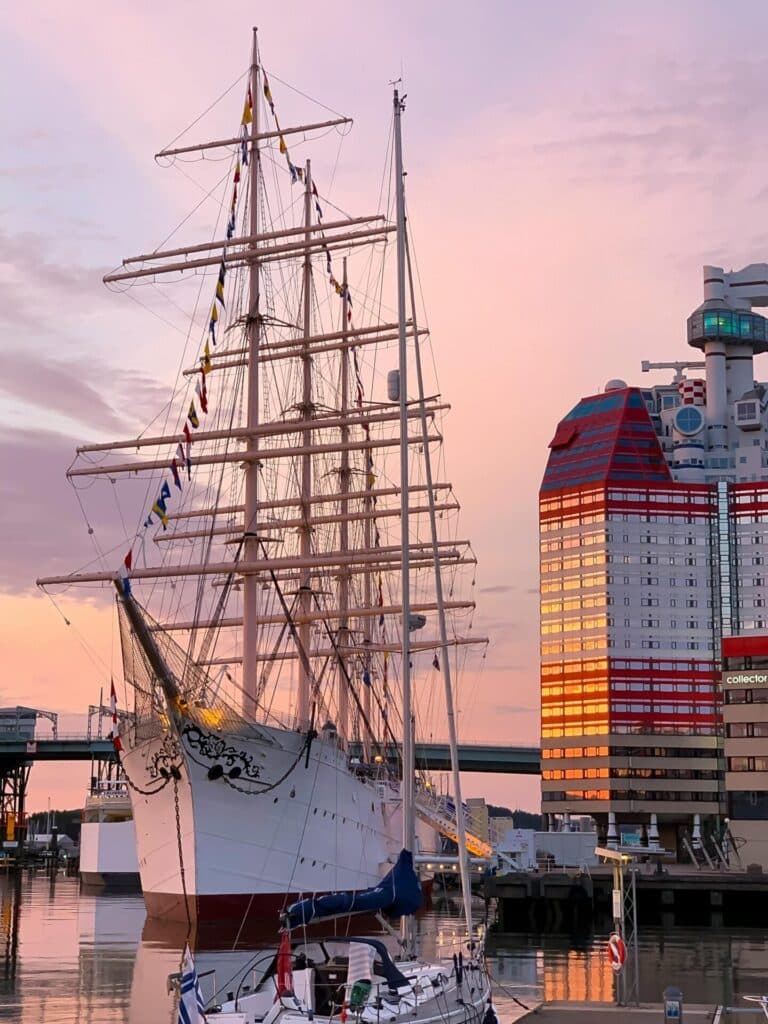 The Barken Viking sailing ship docked in Gothenburg's harbor next to the Läppstiftet building during a colorful sunset.