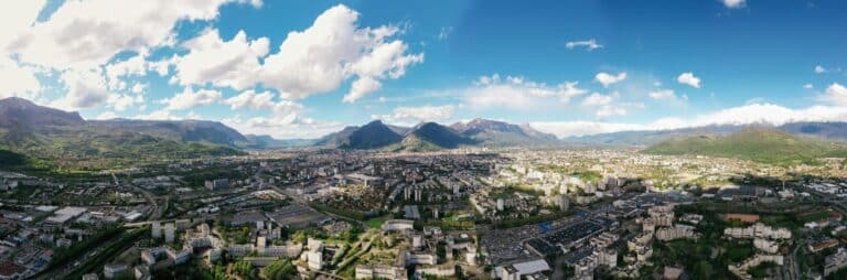 Aerial panorama of the city of Grenoble, France, situated in a valley surrounded by the towering Alps mountains.