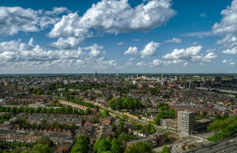 An aerial cityscape view of Groningen under a blue sky with white clouds, showing the Martinitoren in the distance.