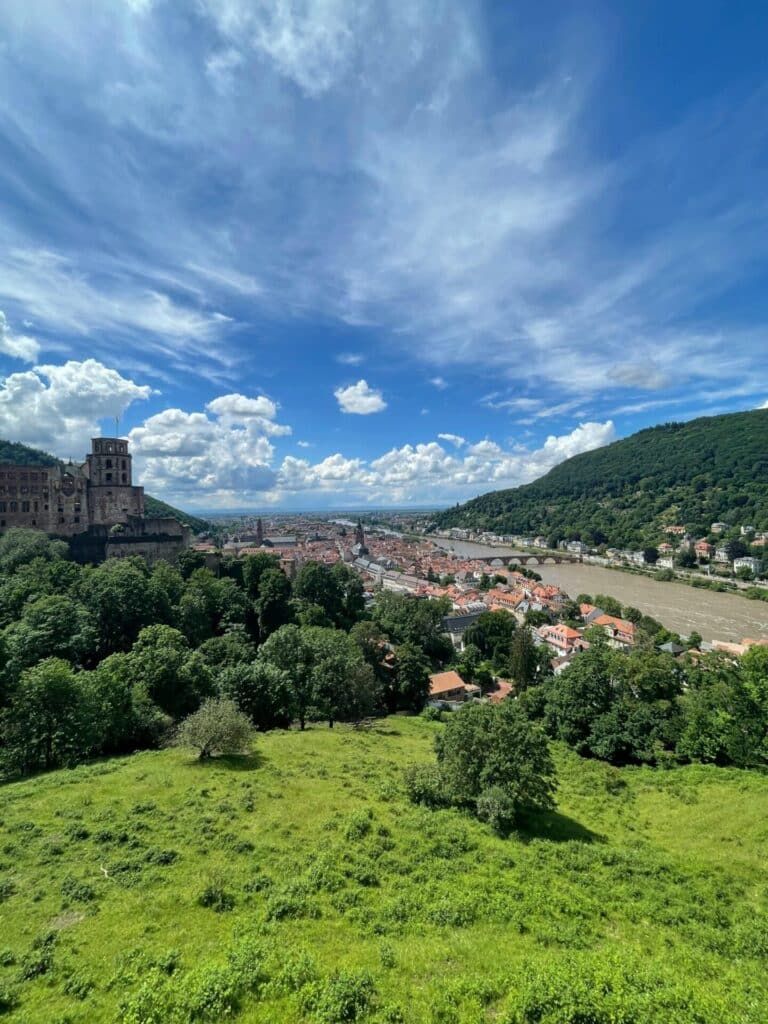 Elevated view of Heidelberg Castle overlooking the Old Town and the Neckar River under a blue, cloudy sky.