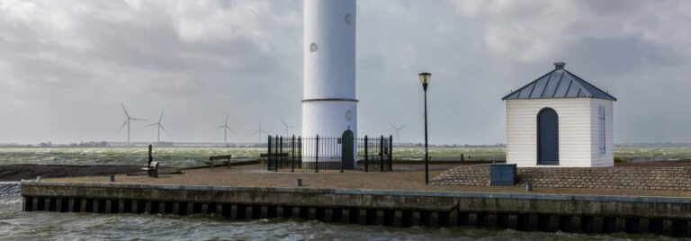 The white Hellevoetsluis Lighthouse with its red top stands on a pier against a dramatic cloudy sky.