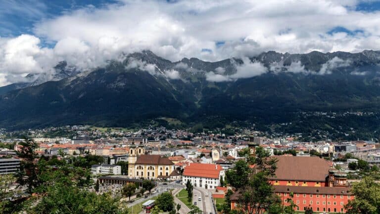 A high-angle view of the city of Innsbruck, Austria, with the dramatic Nordkette mountain range in the background.