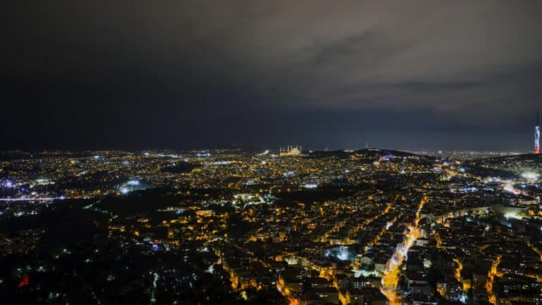 A wide aerial view of the Istanbul cityscape at night, featuring the illuminated Çamlıca Mosque and Çamlıca Tower.