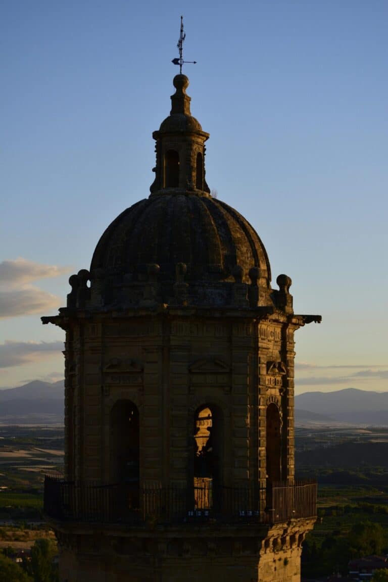 The stone belfry of the Jerez Cathedral bell tower overlooking the Spanish countryside at sunset.