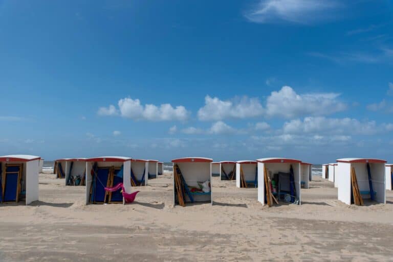 White beach huts with red roofs are lined up on the wide sandy beach in Katwijk aan Zee.