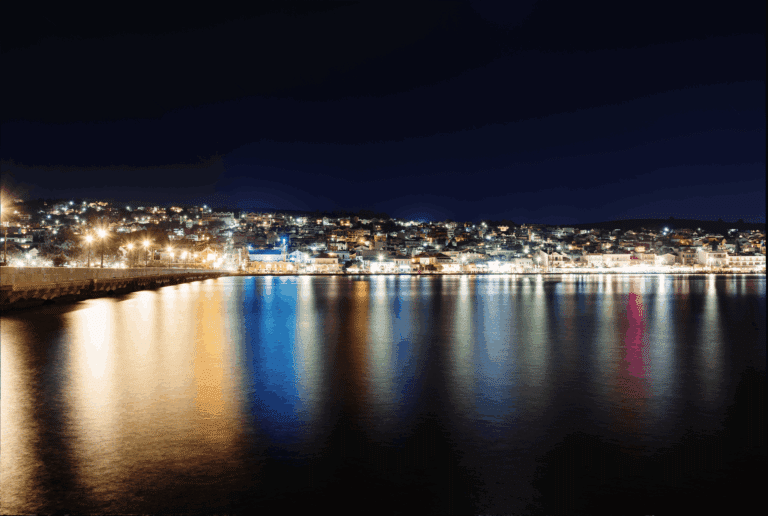 The illuminated harbor of Argostoli in Kefalonia at night, with colorful lights from the town reflecting on the water.