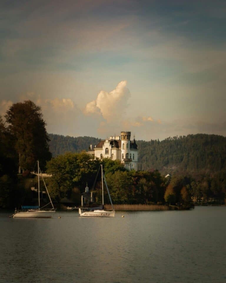 Sailboats float on Lake Wörthersee in front of the historic Schloss Loretto in Klagenfurt, Austria.
