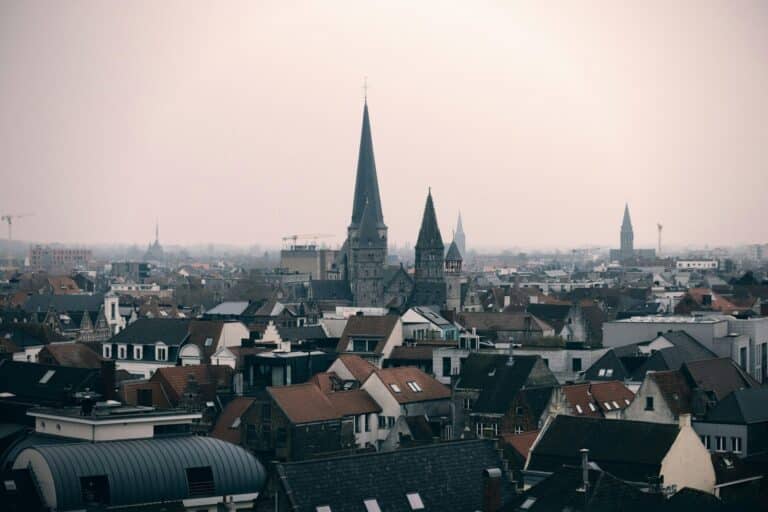 A misty cityscape of Kortrijk showing the many rooftops and the towering spires of Saint Martin's Church.