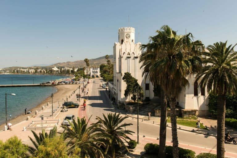 An elevated view of the Governor's Palace, palm trees, and the coastal road along the sea in Kos, Greece.