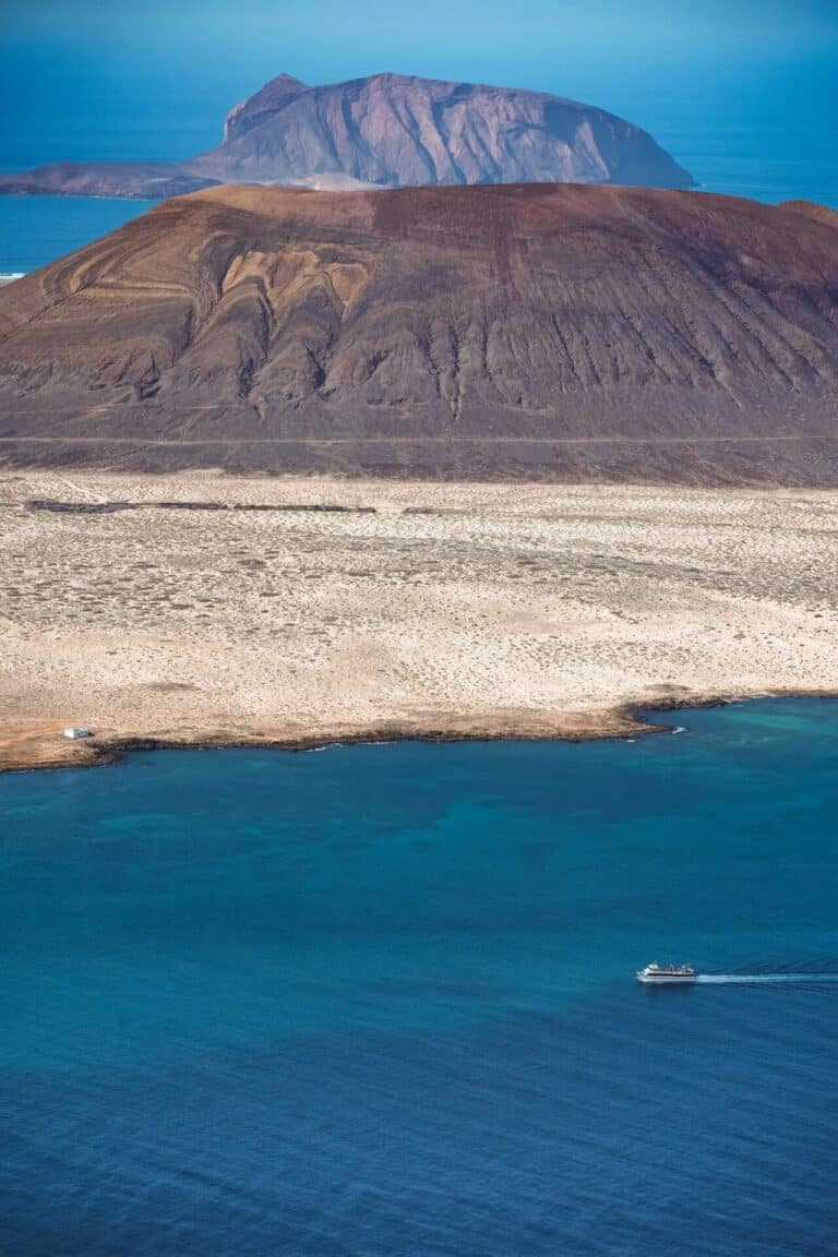 An aerial view from Lanzarote shows the turquoise sea, a ferry boat, and the volcanic island of La Graciosa.