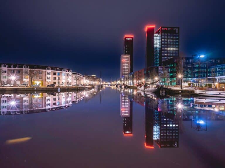 The modern Achmea Tower in Leeuwarden and surrounding buildings reflect in a calm city canal at night.