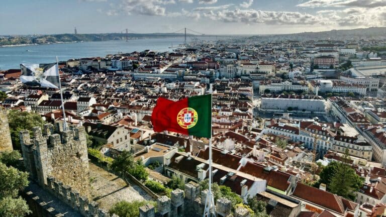 An elevated view of Lisbon from São Jorge Castle, with the Portuguese flag and the Tagus River below.