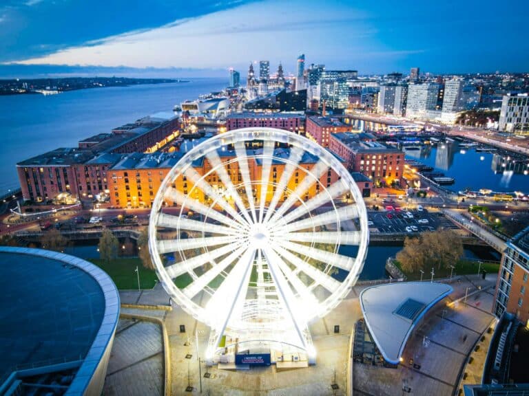 An aerial view of the illuminated Wheel of Liverpool and the Royal Albert Dock with the city skyline at dusk.