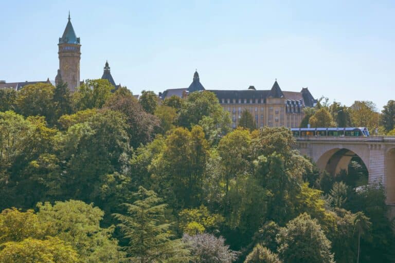 A scenic view of Luxembourg City featuring the Spuerkeess building and a tram crossing the Adolphe Bridge.