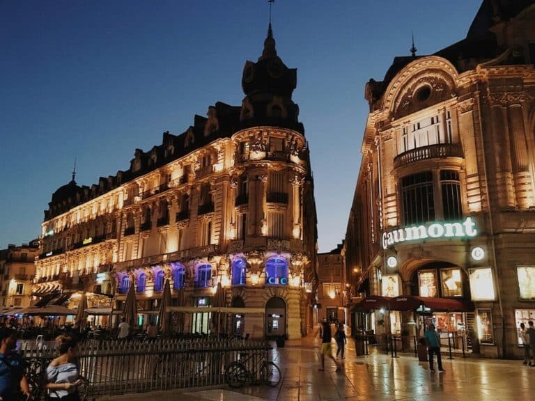 Ornate buildings, including the Gaumont cinema, are illuminated at dusk on the Place de la Comédie in Montpellier.