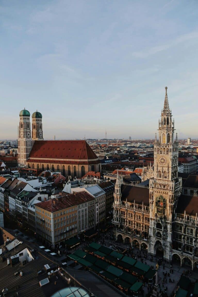 An aerial view of Munich's city center at dusk, featuring the Frauenkirche and the New Town Hall.