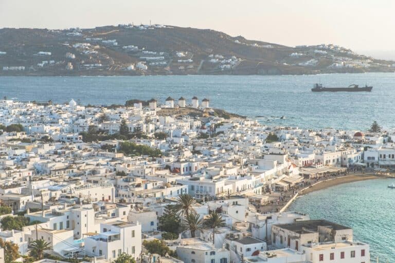 An elevated view of Mykonos town with its white buildings overlooking the Aegean Sea and the Kato Mili windmills.
