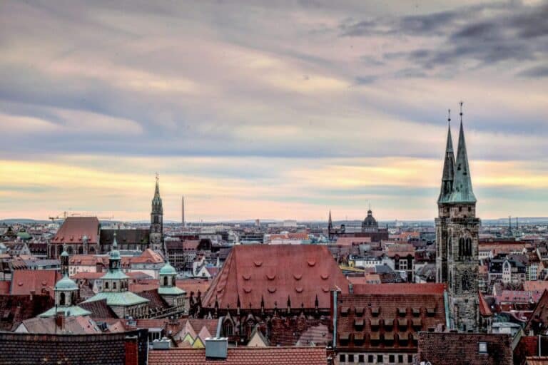 An elevated view over the historic rooftops of Nuremberg, Germany, with St. Lorenz Church prominent at sunset.