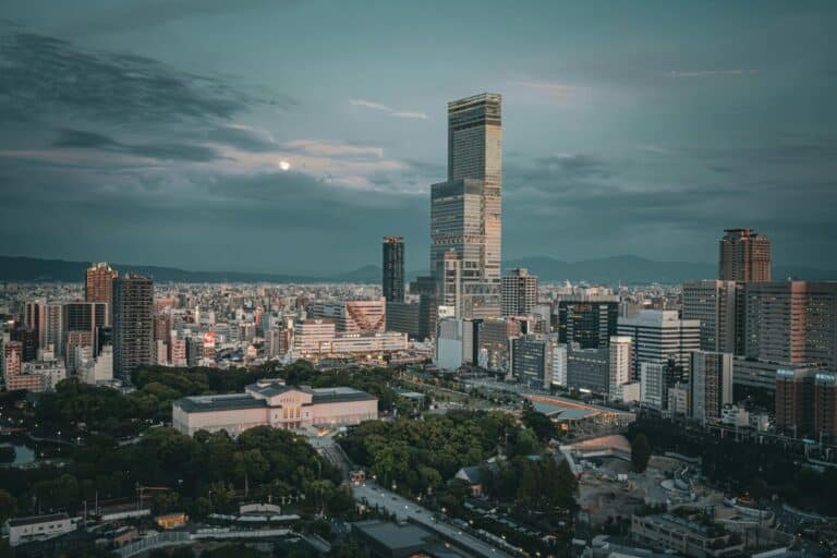 An elevated evening view of the Osaka skyline, featuring the illuminated Abeno Harukas skyscraper and Tennoji Park.