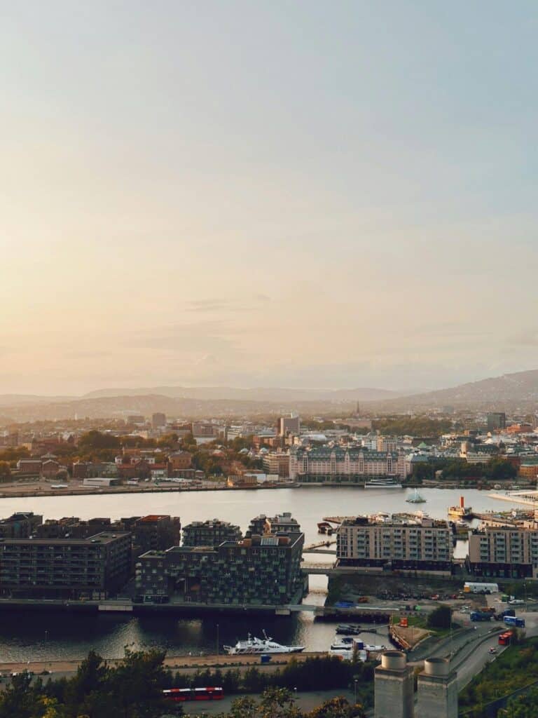 An elevated view of Oslo's modern Tjuvholmen district and waterfront against the city skyline at sunset.