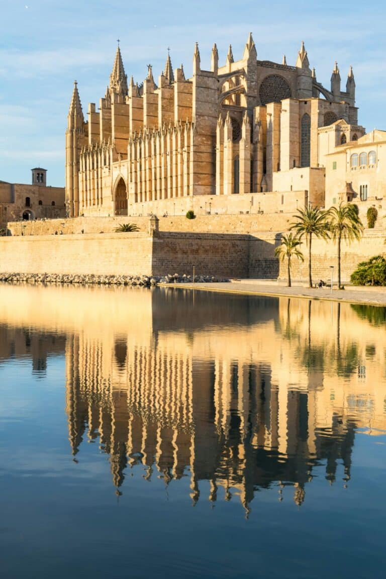 The grand Cathedral of Palma de Mallorca stands over a placid lake, its golden facade perfectly reflected in the water.