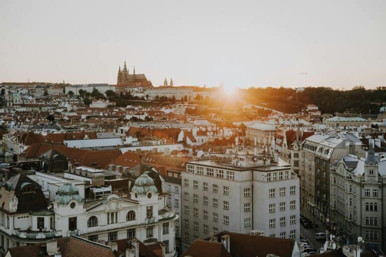 An elevated view over the red rooftops of Prague with the Prague Castle complex on the hill at sunset.