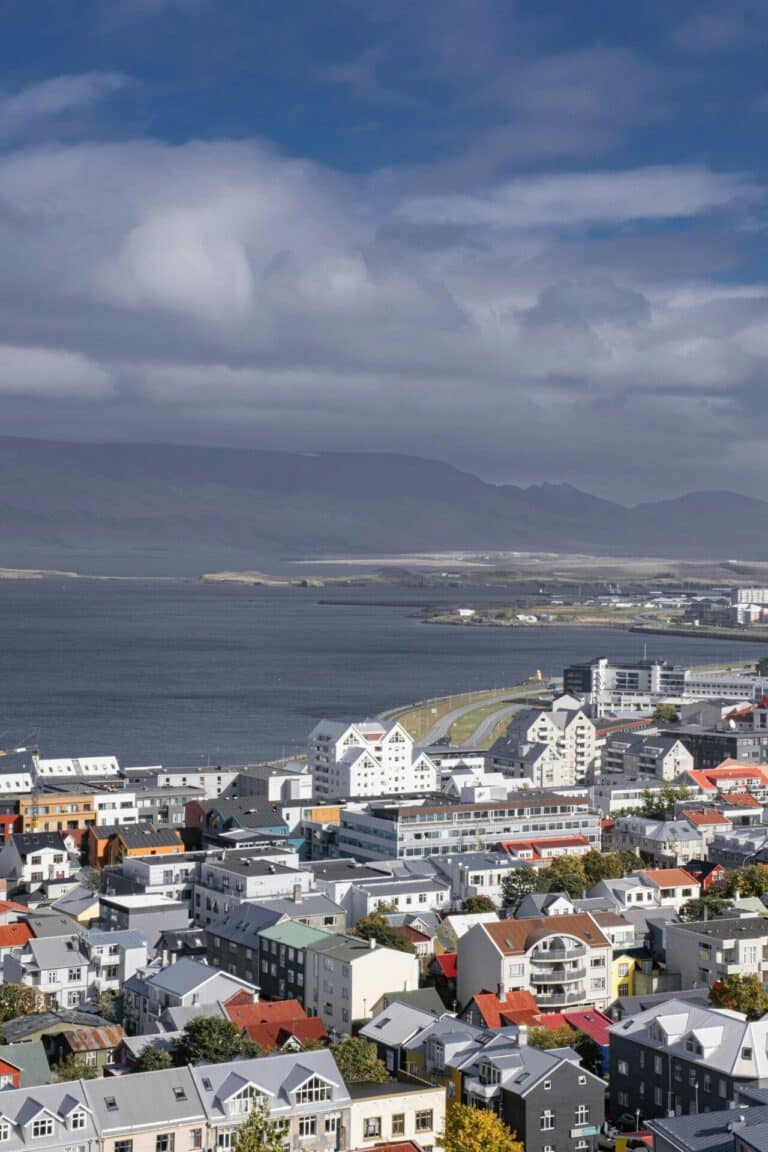 An aerial view of Reykjavik's colorful houses and buildings, with the bay and distant mountains in the background.