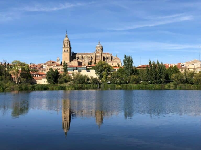 The skyline of Salamanca with its grand cathedral reflected in the calm waters of the Tormes River.