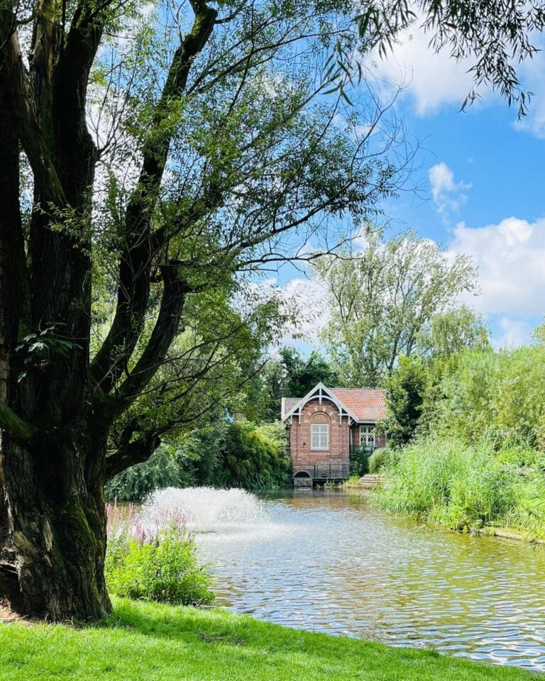 A historic brick pumping station with a red tile roof sits by the water in Springerpark, Schoonhoven.