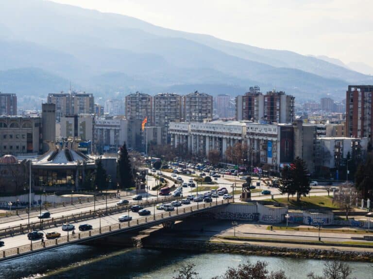 A high-angle daytime view of Skopje, showing traffic on the Goce Delčev Bridge over the Vardar River.